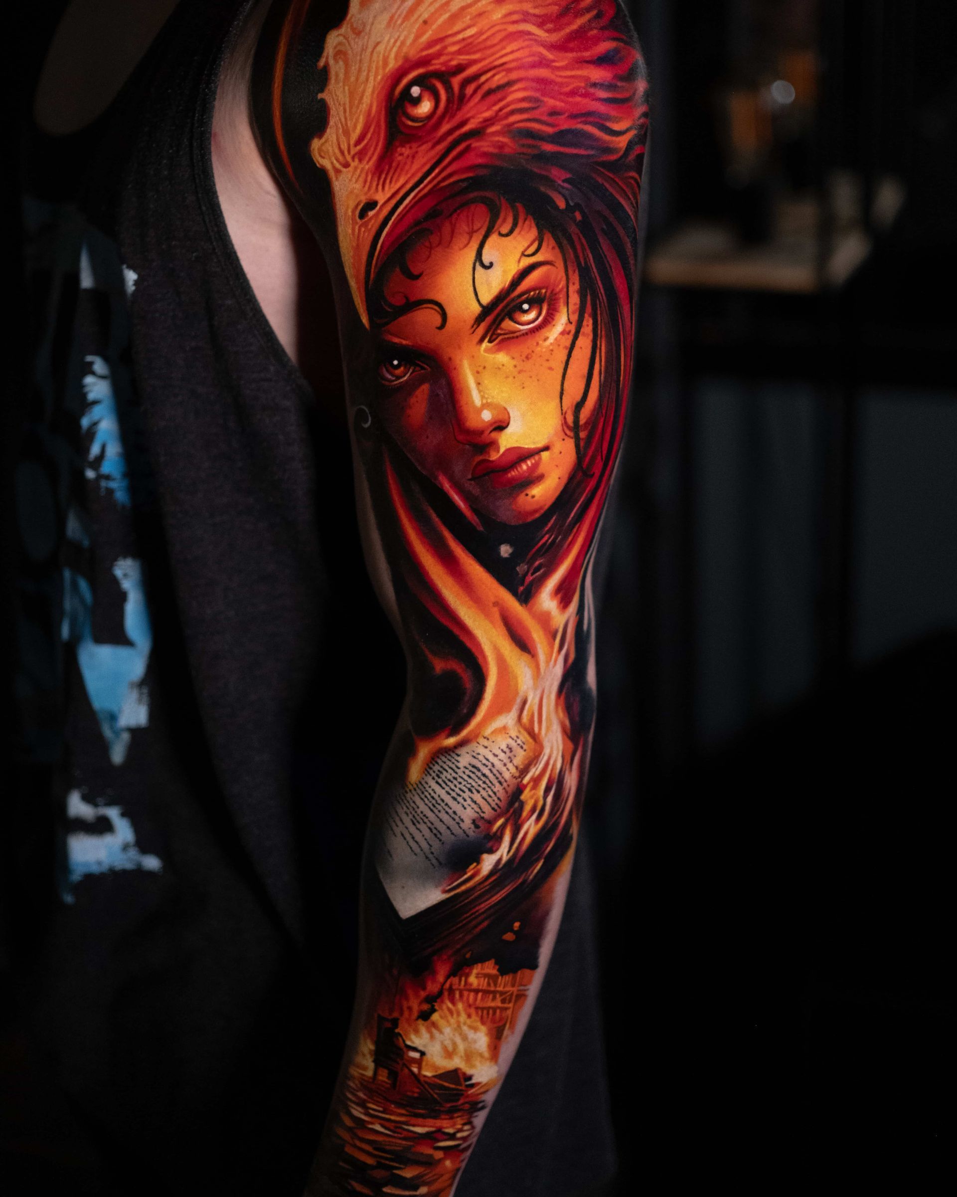 A vibrant, realistic tattoo on an arm featuring a woman’s face framed by an eagle and flames in orange and crimson tones.