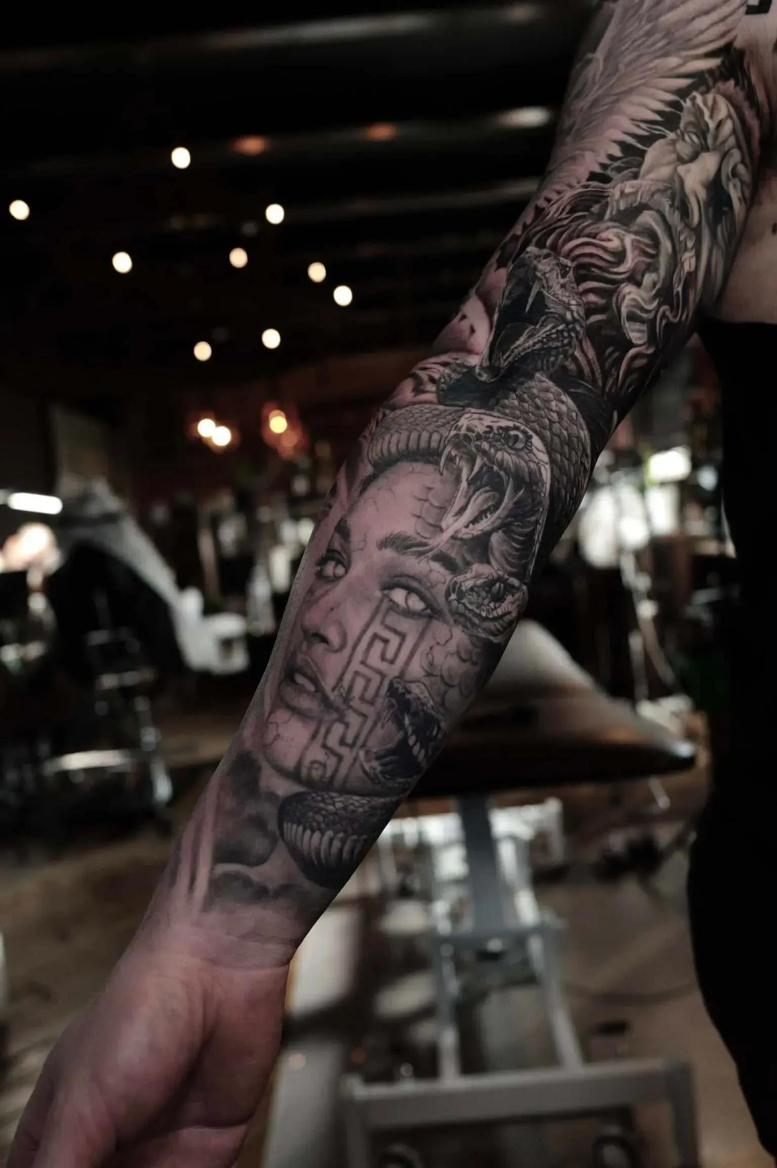 A detailed black-and-grey tattoo on a person's forearm featuring a portrait of Medusa surrounded by snakes.