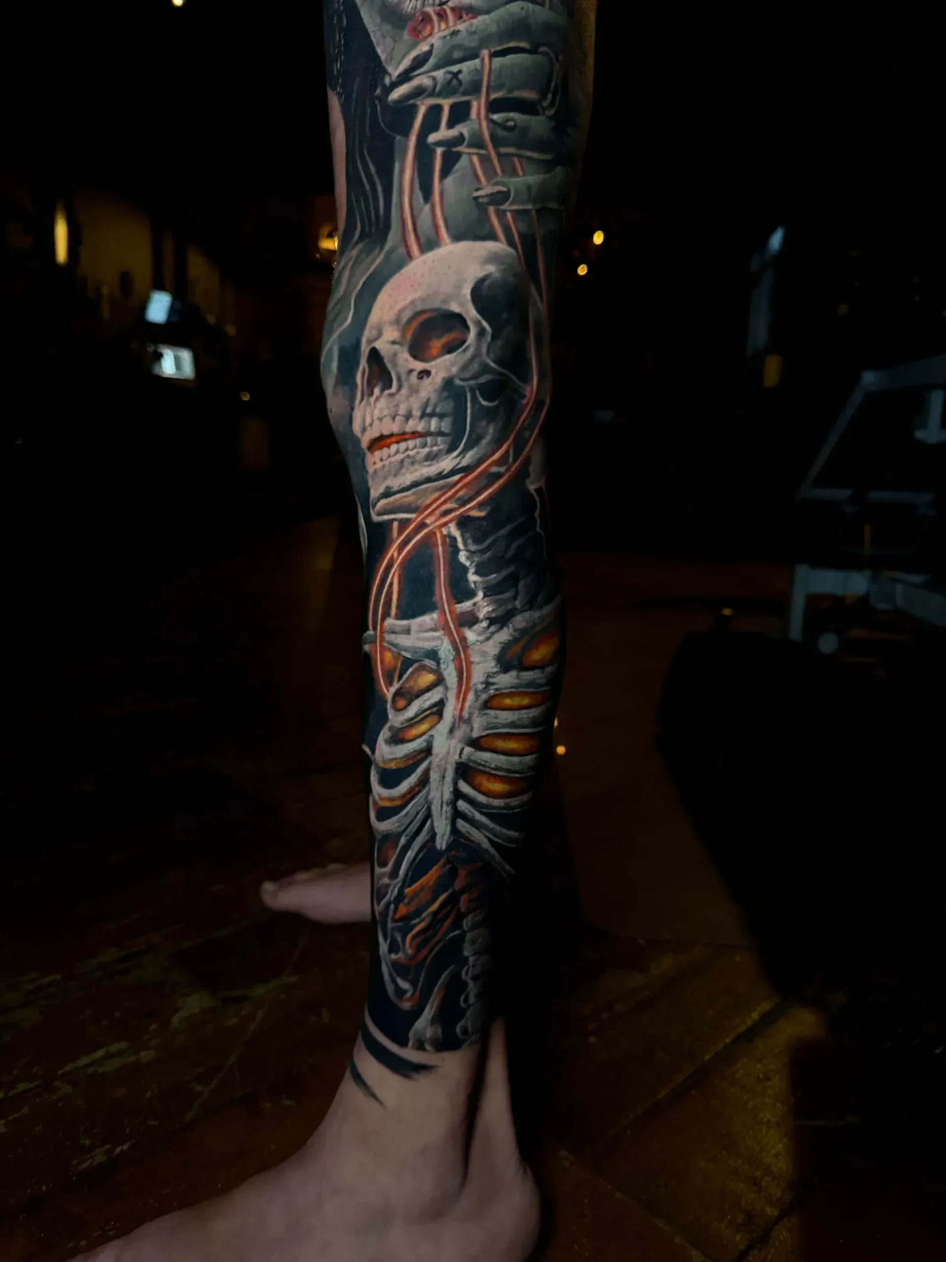 A detailed tattoo of a skull and ribcage on a person's lower leg, featuring glowing orange chains and dark shading.