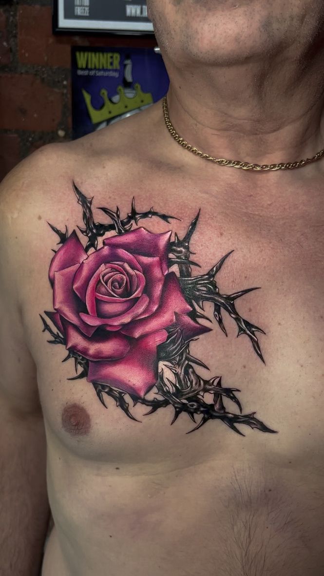 A vibrant magenta rose surrounded by dark, sharp thorns tattooed on a person's upper right chest.