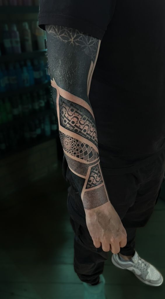 Person's arm showing a blackwork sleeve tattoo with geometric, lace-like patterns and negative space cutouts.