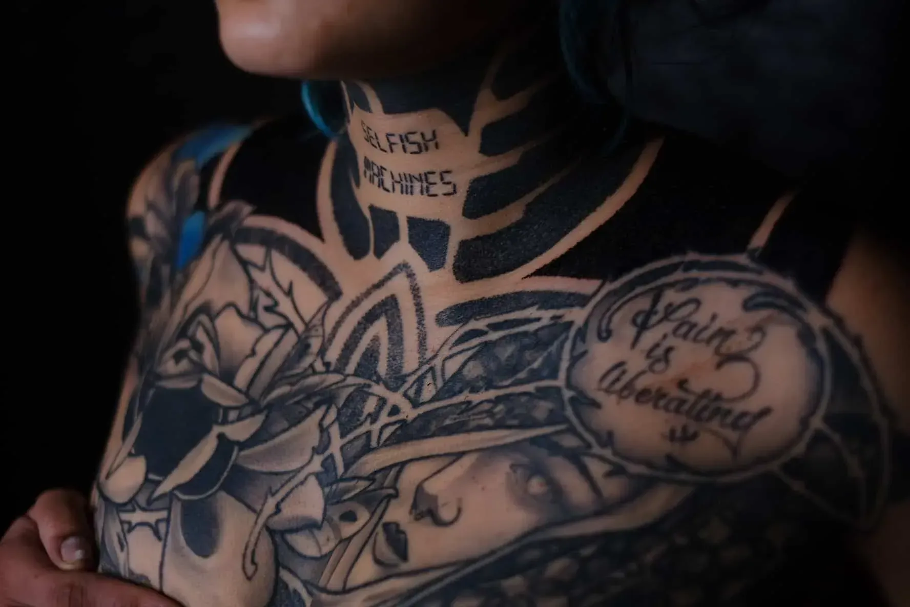 A close-up of neck and chest tattoos, including a throat inscription reading