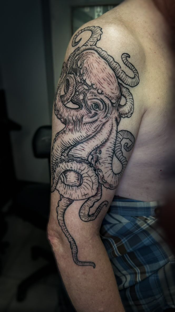 An octopus tattoo with detailed black linework and shading covering the upper arm.