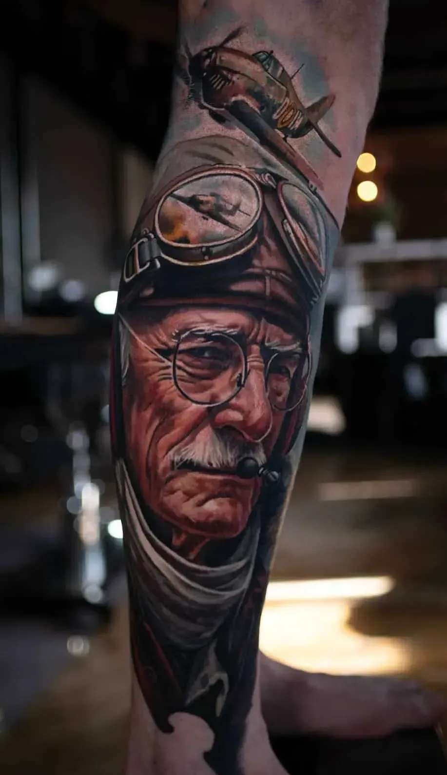Detailed tattoo on a lower leg featuring a vintage aviator wearing goggles and glasses, with a small plane above him.