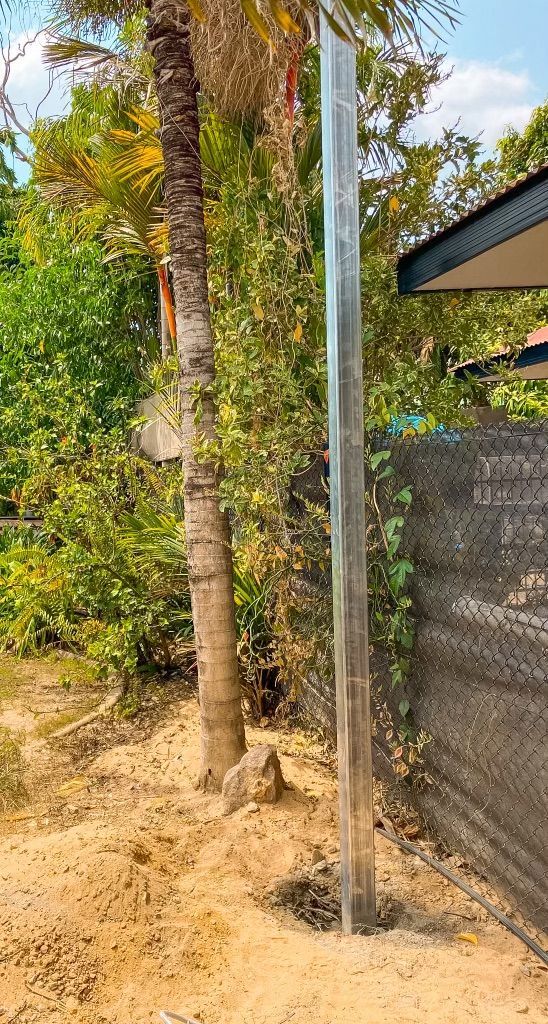 A Metal Pole is Sitting in the Dirt Next to a Palm Tree — Fewmore Contracting in Yarrawonga, NT