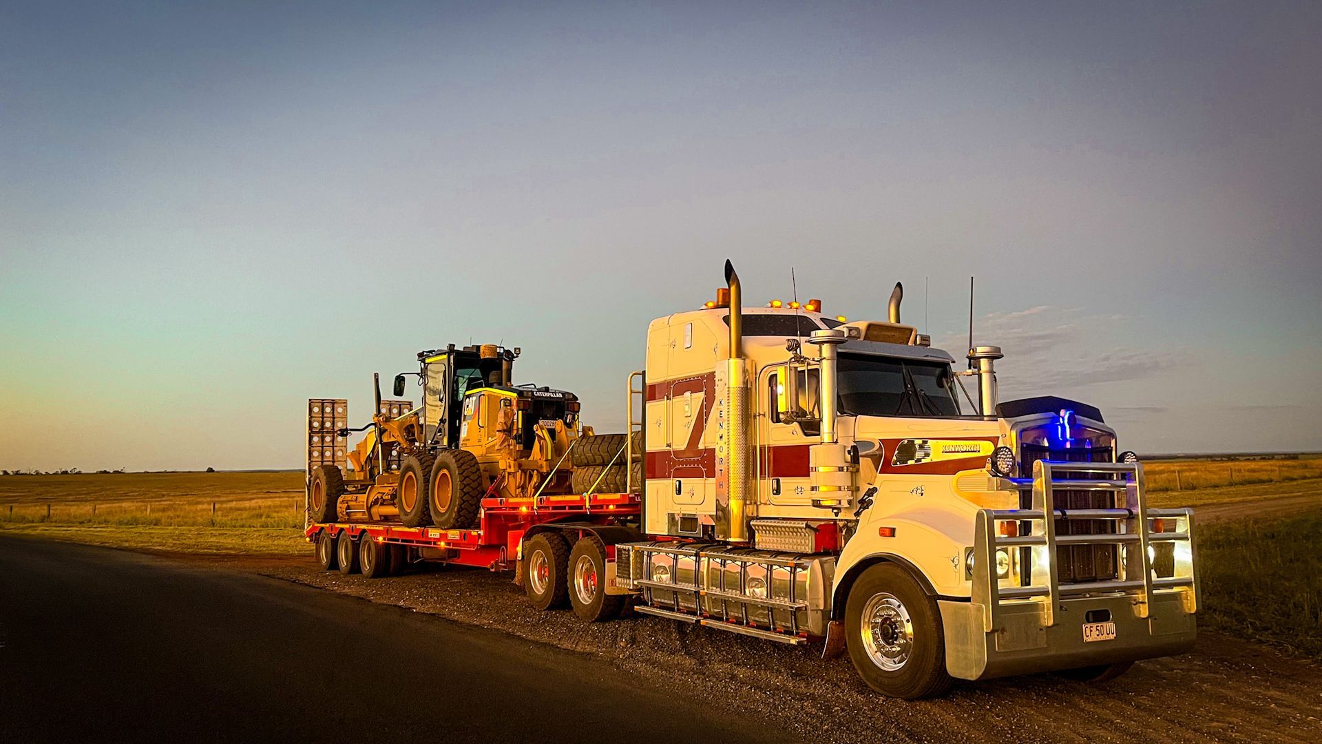 A Semi Truck is Carrying a Bulldozer Down a Dirt Road — Fewmore Contracting In Tennant Creek, NT