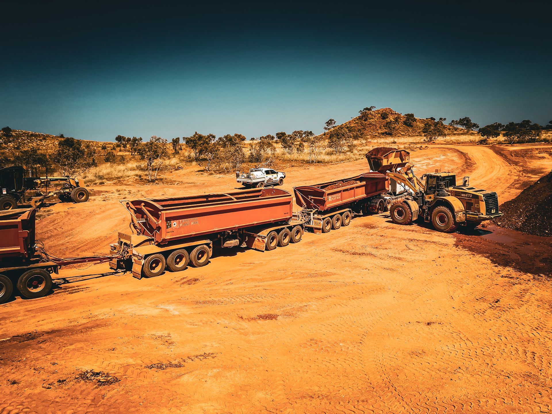 A Dump Truck is Being Towed by a Bulldozer on a Dirt Road — Fewmore Contracting in Katherine, NT