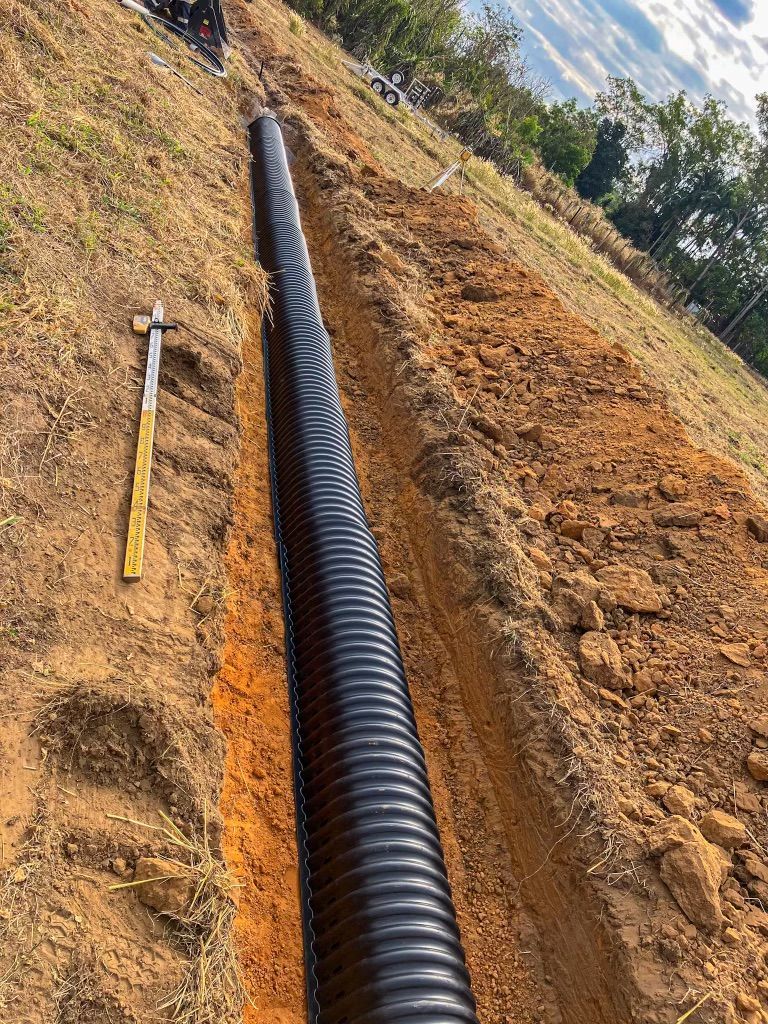 A Large Black Pipe is Being Installed in the Dirt Next to a Shovel — Fewmore Contracting In Tennant Creek, NT