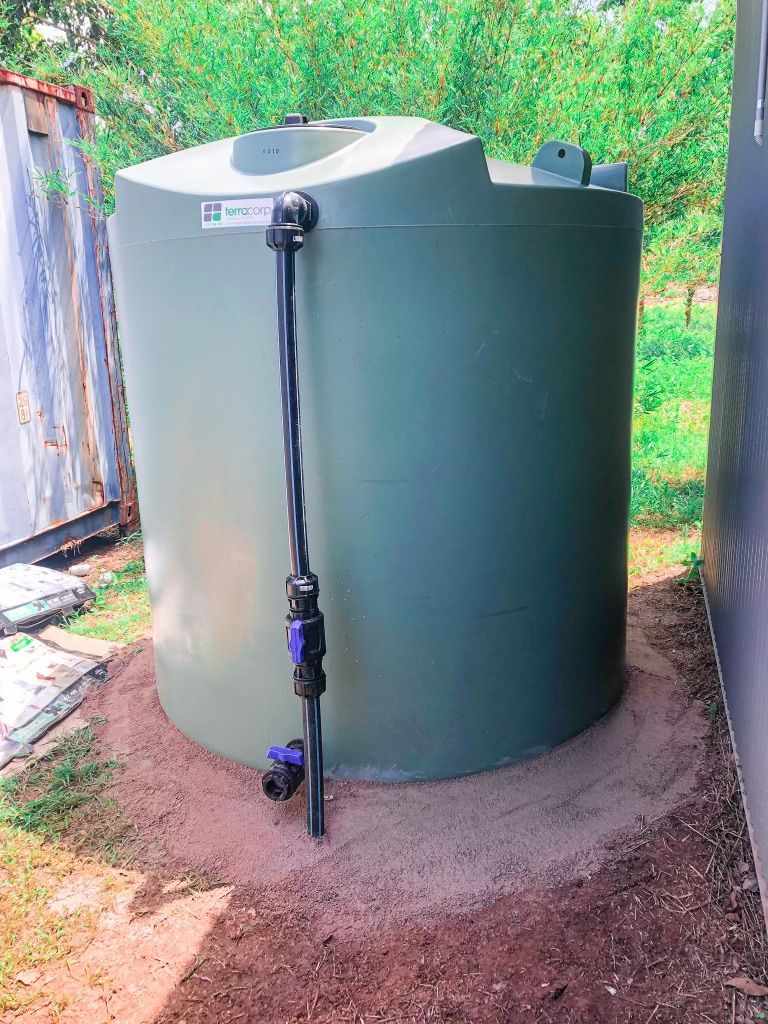 A Large Green Water Tank is Sitting in the Dirt Next to a Building — Fewmore Contracting in Katherine, NT