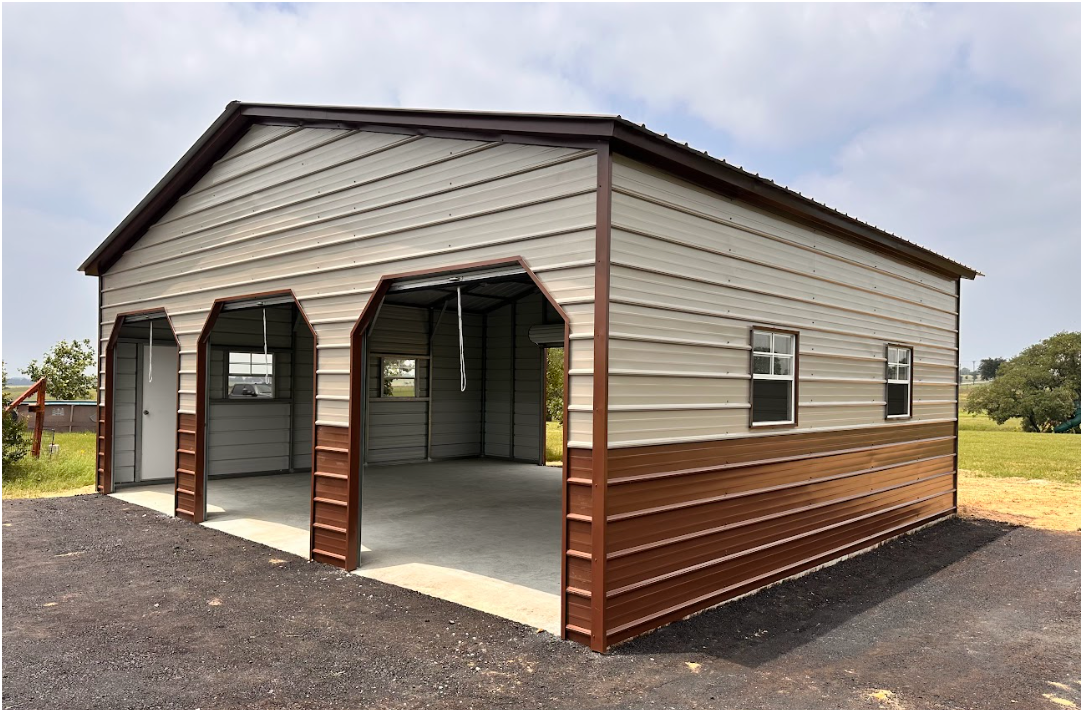A beige and brown metal garage building with two open bays and a side entry door, set on a gravel lot under a blue sky.
