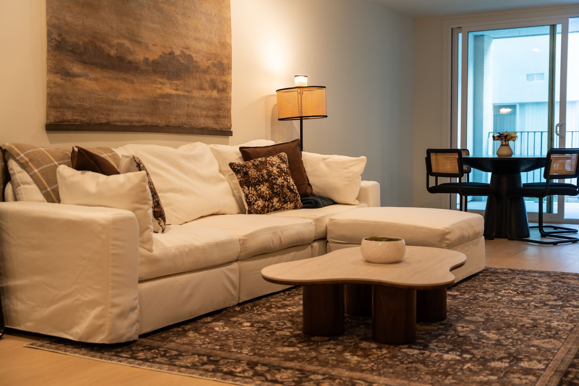 Living room with white sectional sofa, patterned rug, coffee table, art, and dining area.