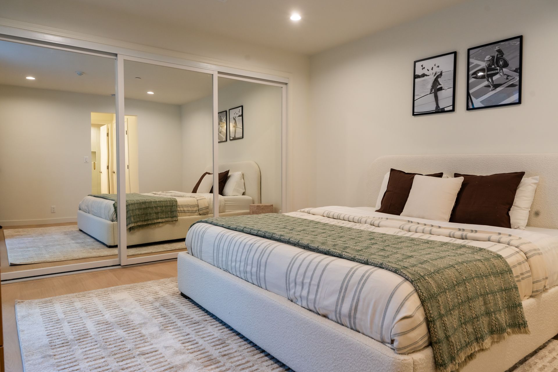 Bedroom with white walls, a bed with a green blanket, and a mirrored closet. Two framed pictures on the wall.