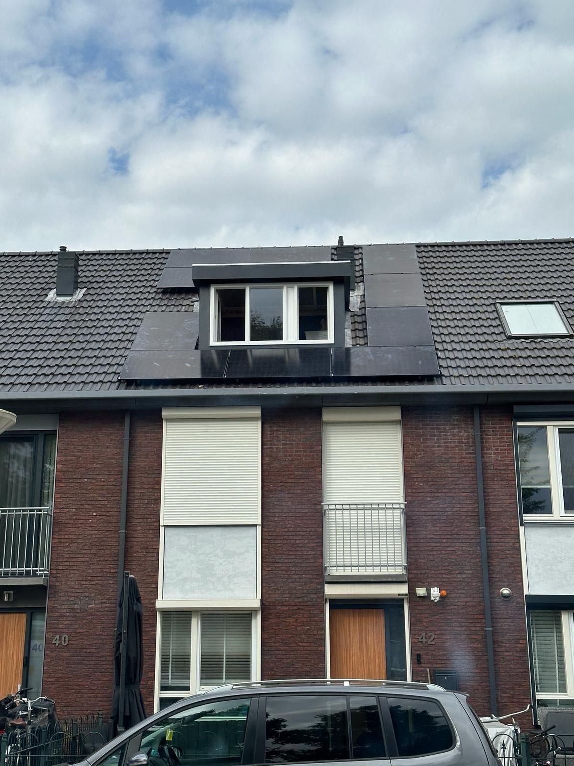 Er staat een auto geparkeerd voor een bakstenen gebouw met zonnepanelen op het dak.