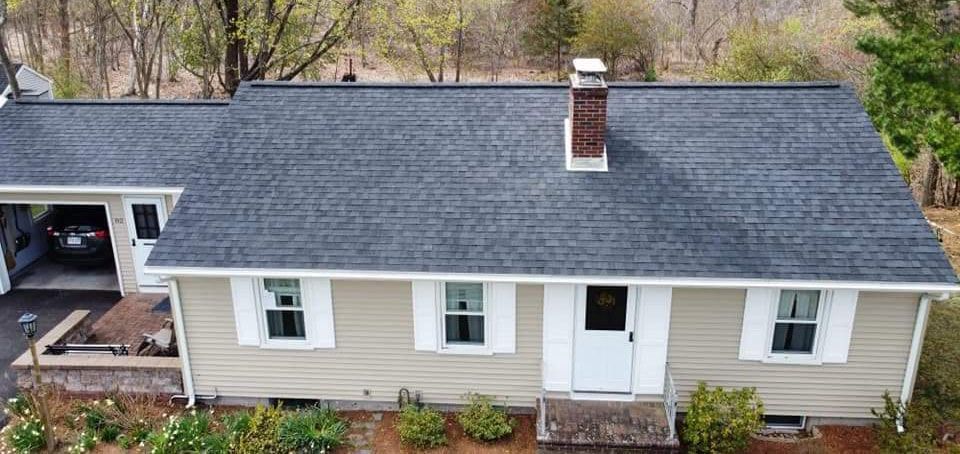 Overhead view of a light-beige house with a dark-gray roof, white trim, and a carport.