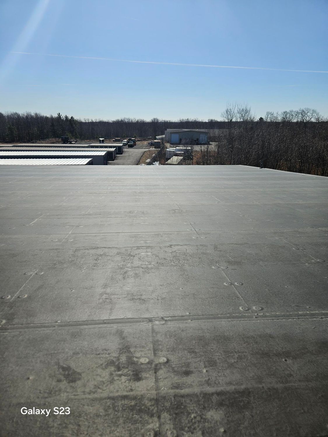 Flat, dark roof with a view of a distant road, buildings, and trees under a bright blue sky.