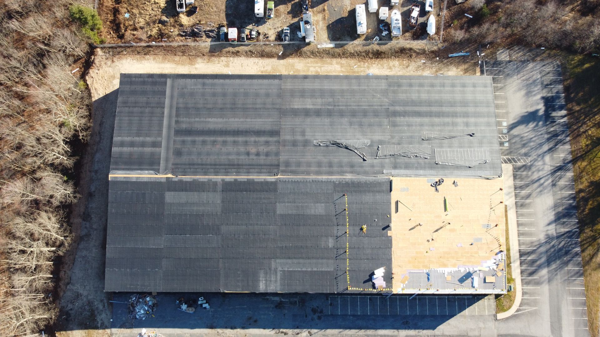Aerial view of a damaged black industrial roof with visible cracks and missing sections.