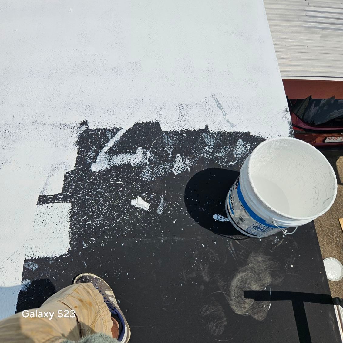 Painted rooftop surface with a white bucket and a person’s shoe visible near the bottom left