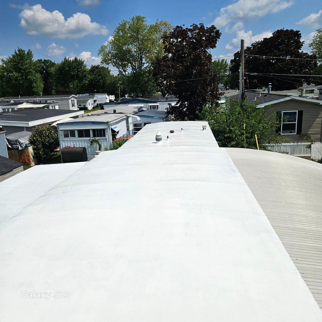 White rooftop overlooking a mobile home park with trees and clear blue sky