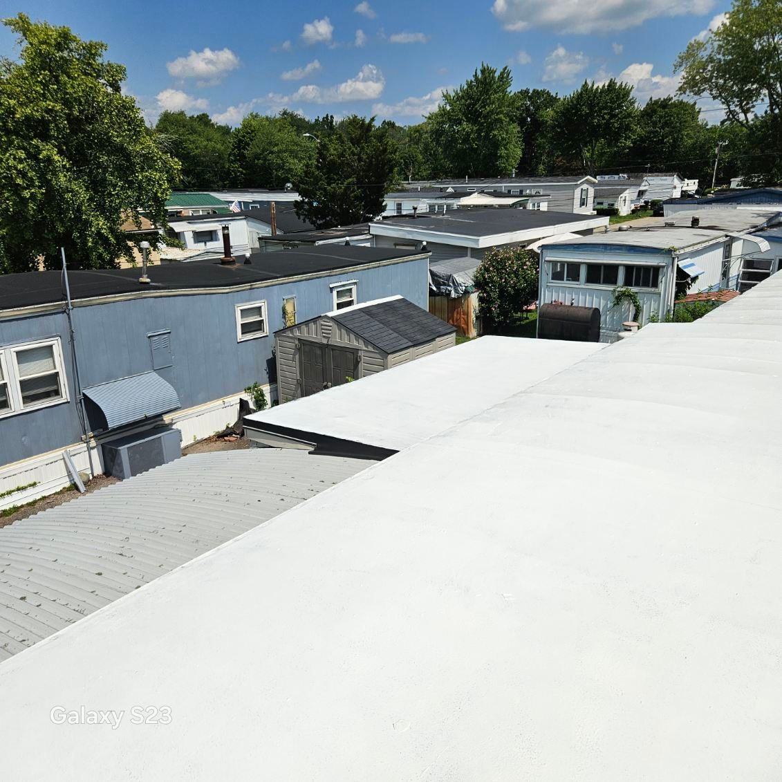 White rooftop overlooking gray mobile homes and green trees under a blue sky