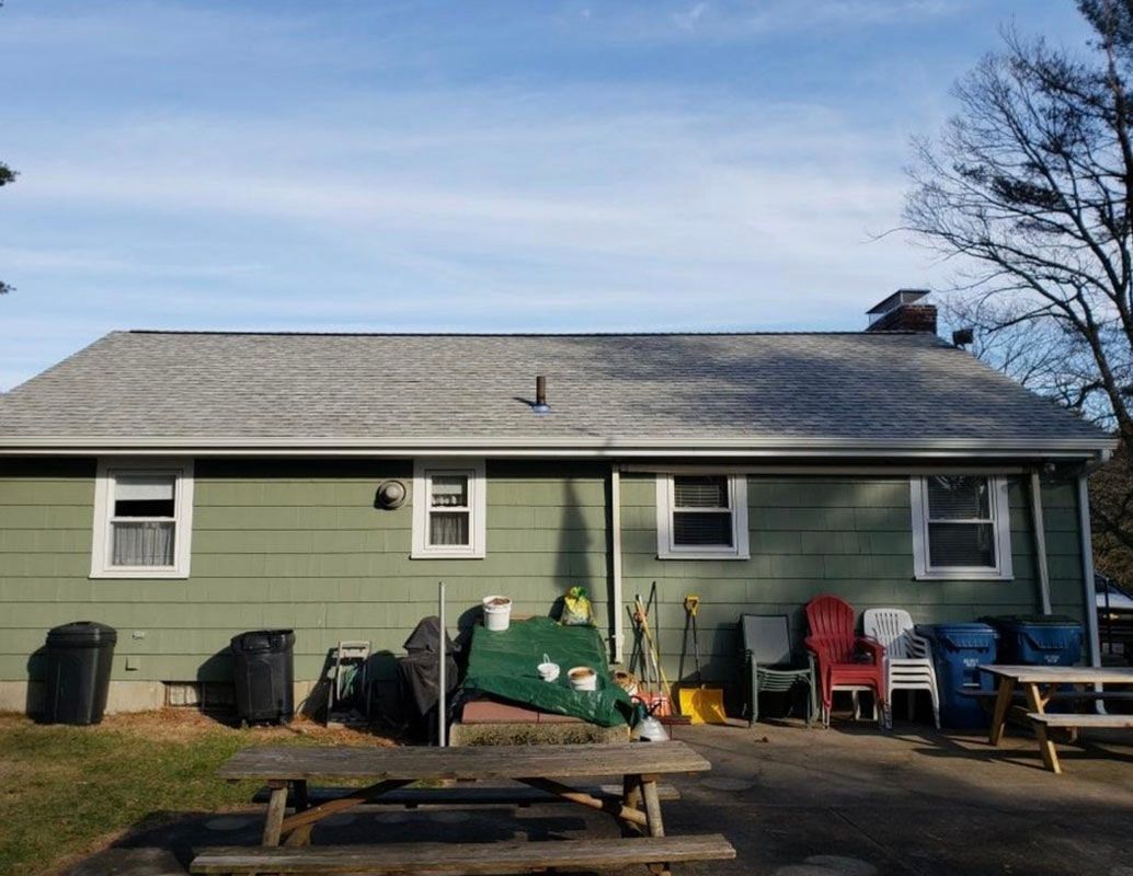 Green house exterior with picnic table, chairs, and trash cans on a sunny day.