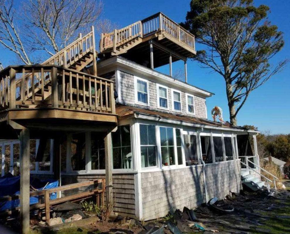 Coastal house with multiple decks and stairs, weathered shingles, and a blue sky.