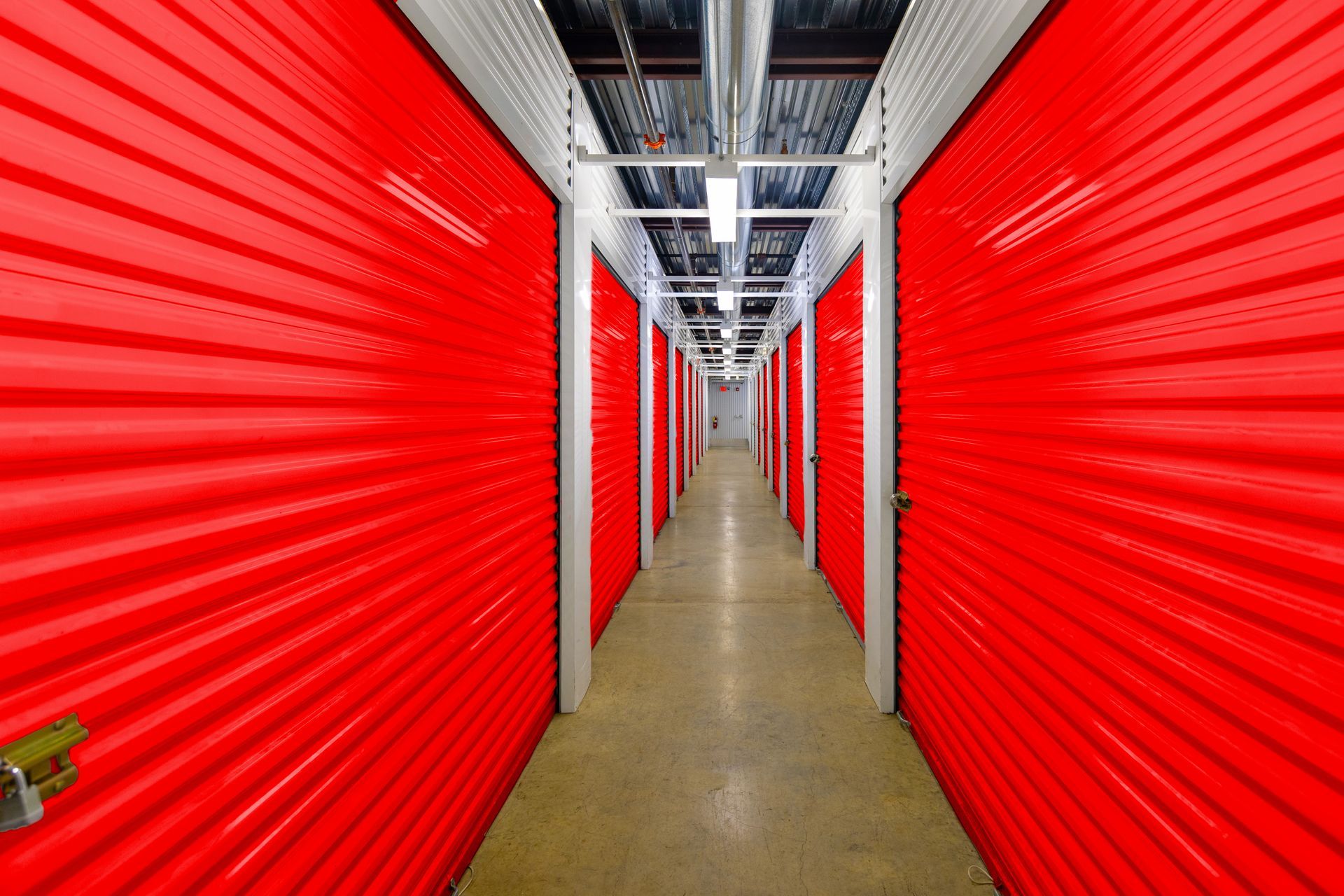Indoor climate-controlled self storage units with red roll-up doors in clean facility hallway.