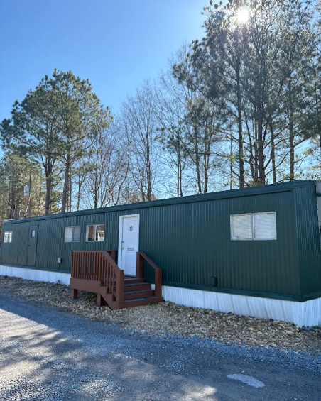 Armuchee Self Storage facility exterior in Rome, Georgia, featuring a green metal building with wooden entrance steps surrounded by pine trees