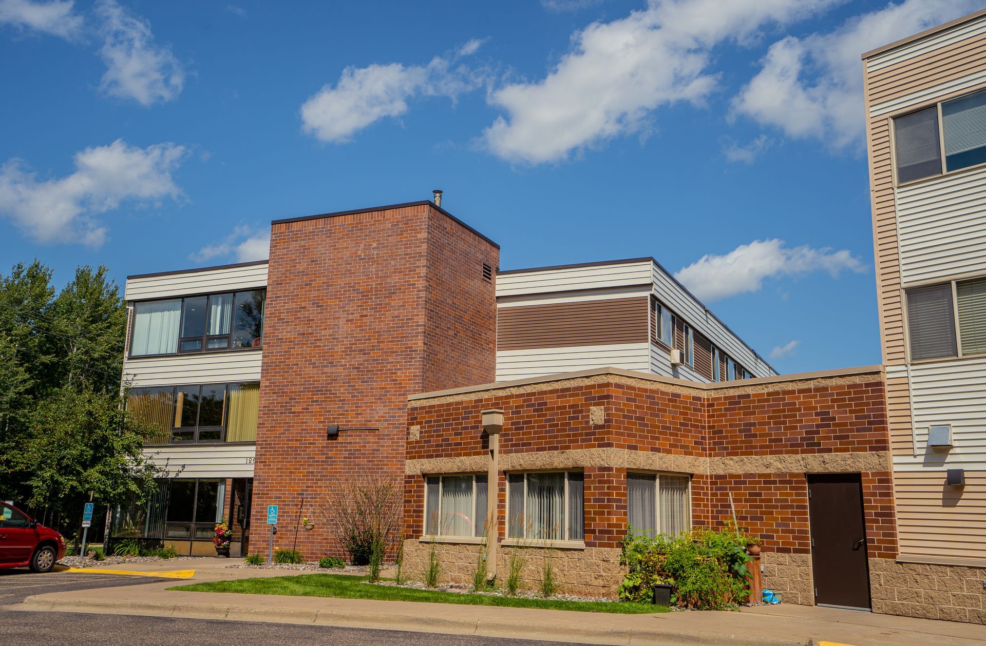 A multi-story building featuring red brick, patterned siding, and several windows under a sunny blue sky.