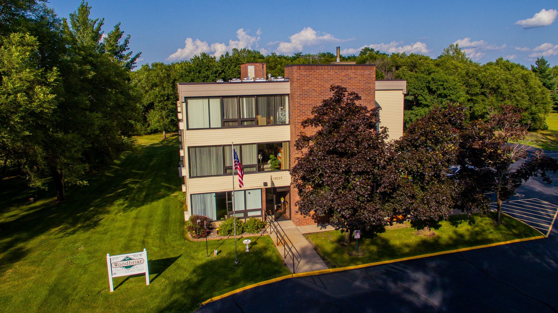A three-story building with a brick facade and large windows, surrounded by trees and a green lawn under a blue sky.