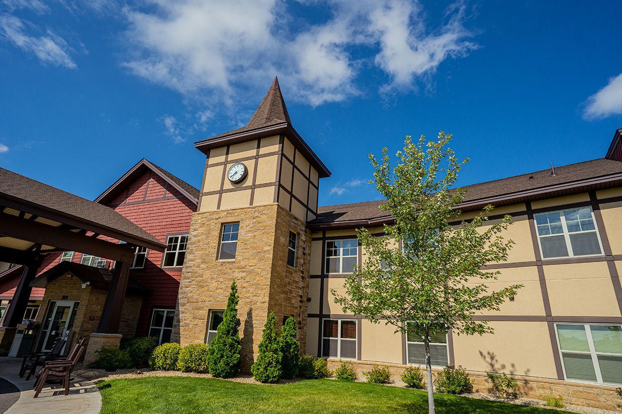 A multi-story building with timber-frame siding, stone accents, and a clock tower under a bright blue sky.