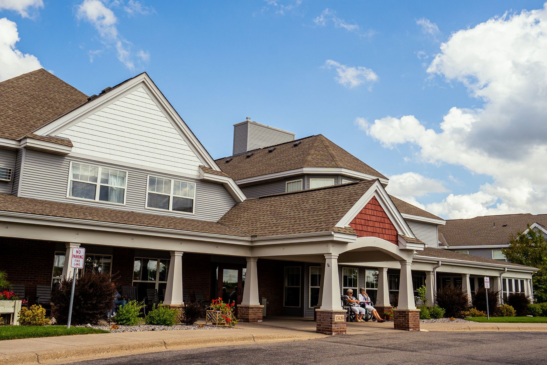 A multi-story building with a brown shingled roof, cream-colored siding, and a covered entrance area on a sunny day.