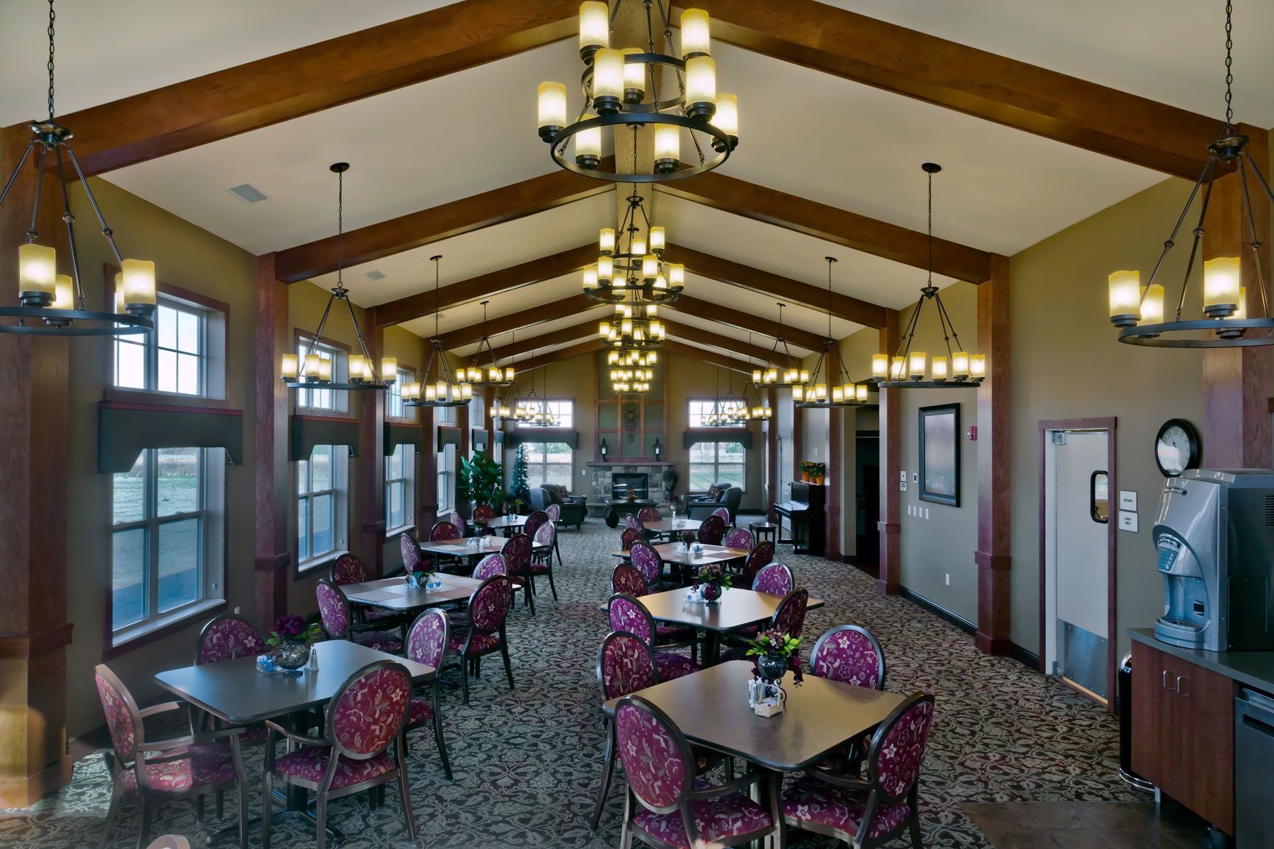 A spacious dining room with vaulted wood-beamed ceilings, multiple chandeliers, and rows of tables with patterned chairs.