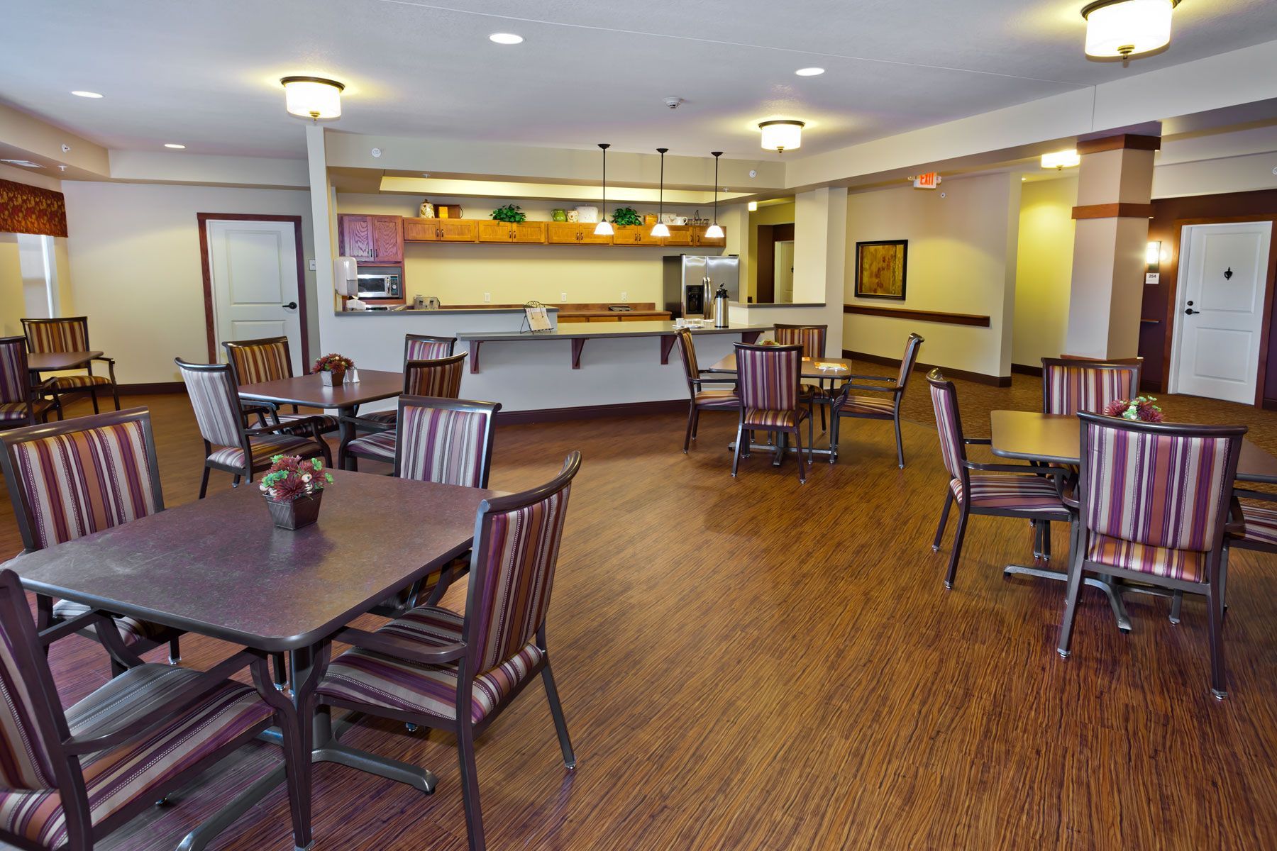 A dining room with wood-patterned flooring, tables with striped chairs, and a bar area with pendant lighting.