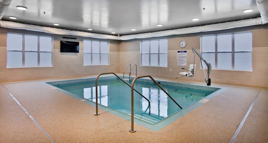 Indoor pool with a beige floor, surrounding tan walls, and a mechanical accessibility lift on the right side.