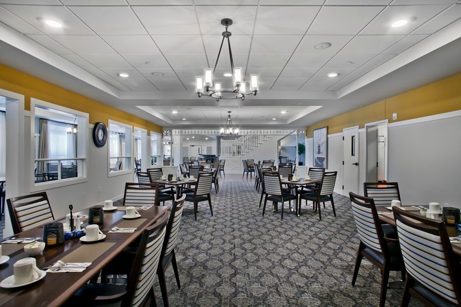 A dining hall featuring rows of wooden tables, patterned grey carpet, yellow walls, and hanging chandeliers.