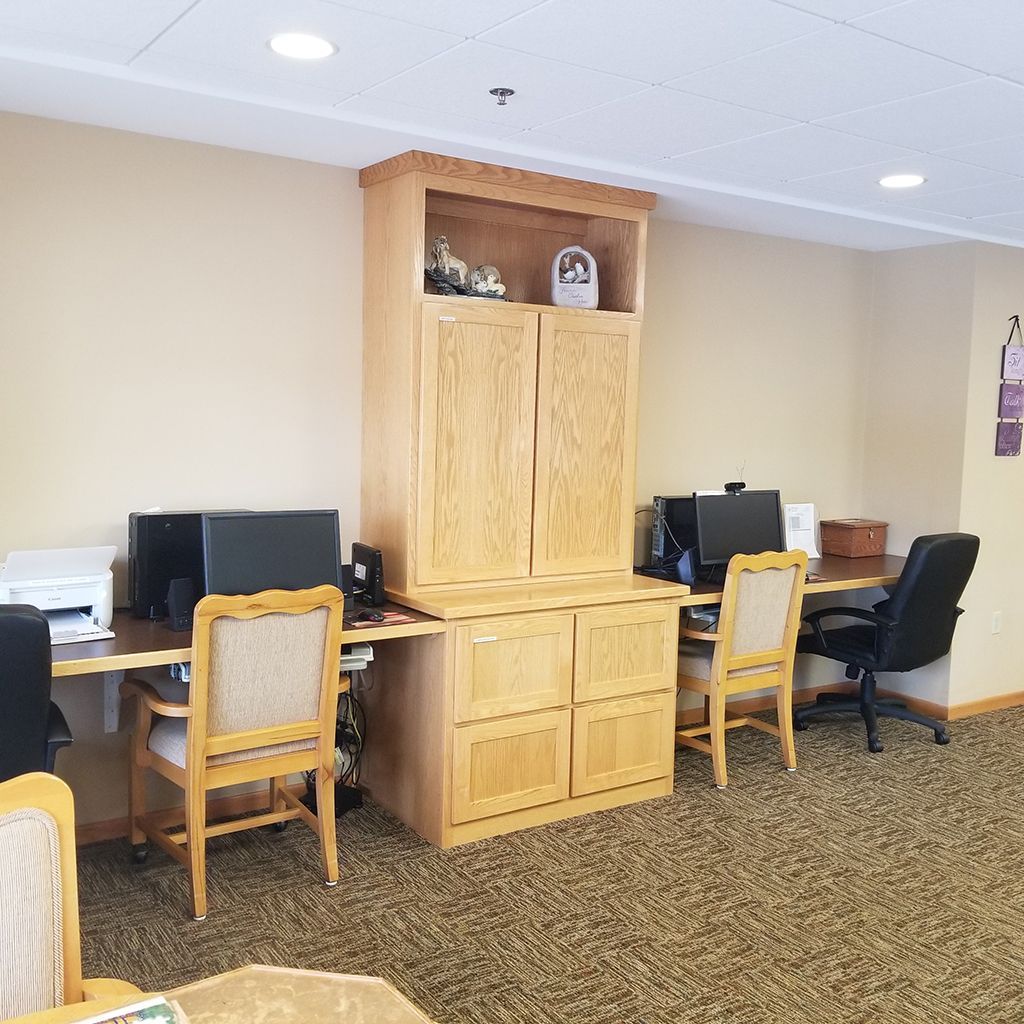 A shared computer workspace featuring light-wood cabinetry, two workstations with monitors, and fabric-upholstered chairs.