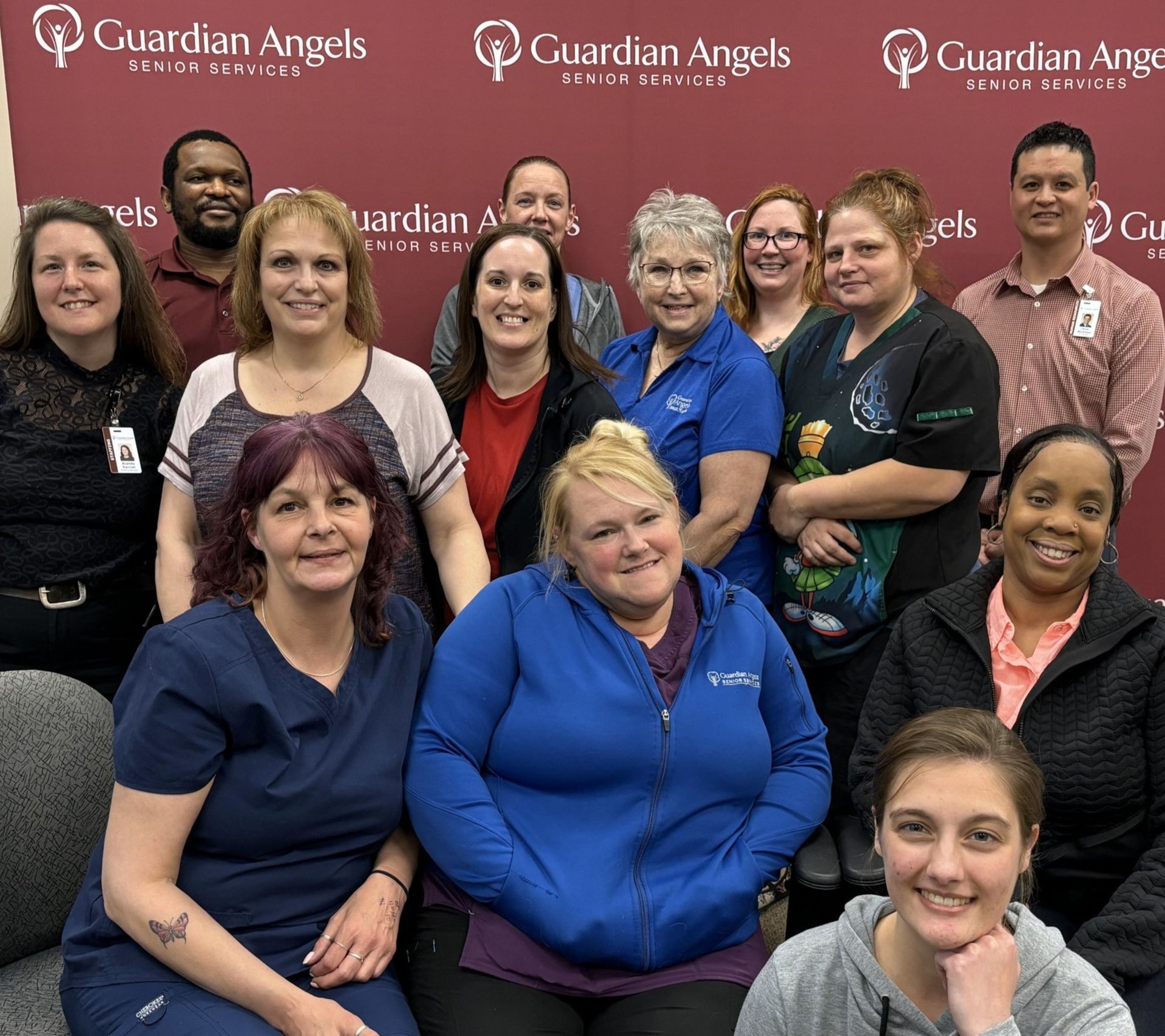 A group photo of thirteen people posing in front of a maroon Guardian Angels brand backdrop.
