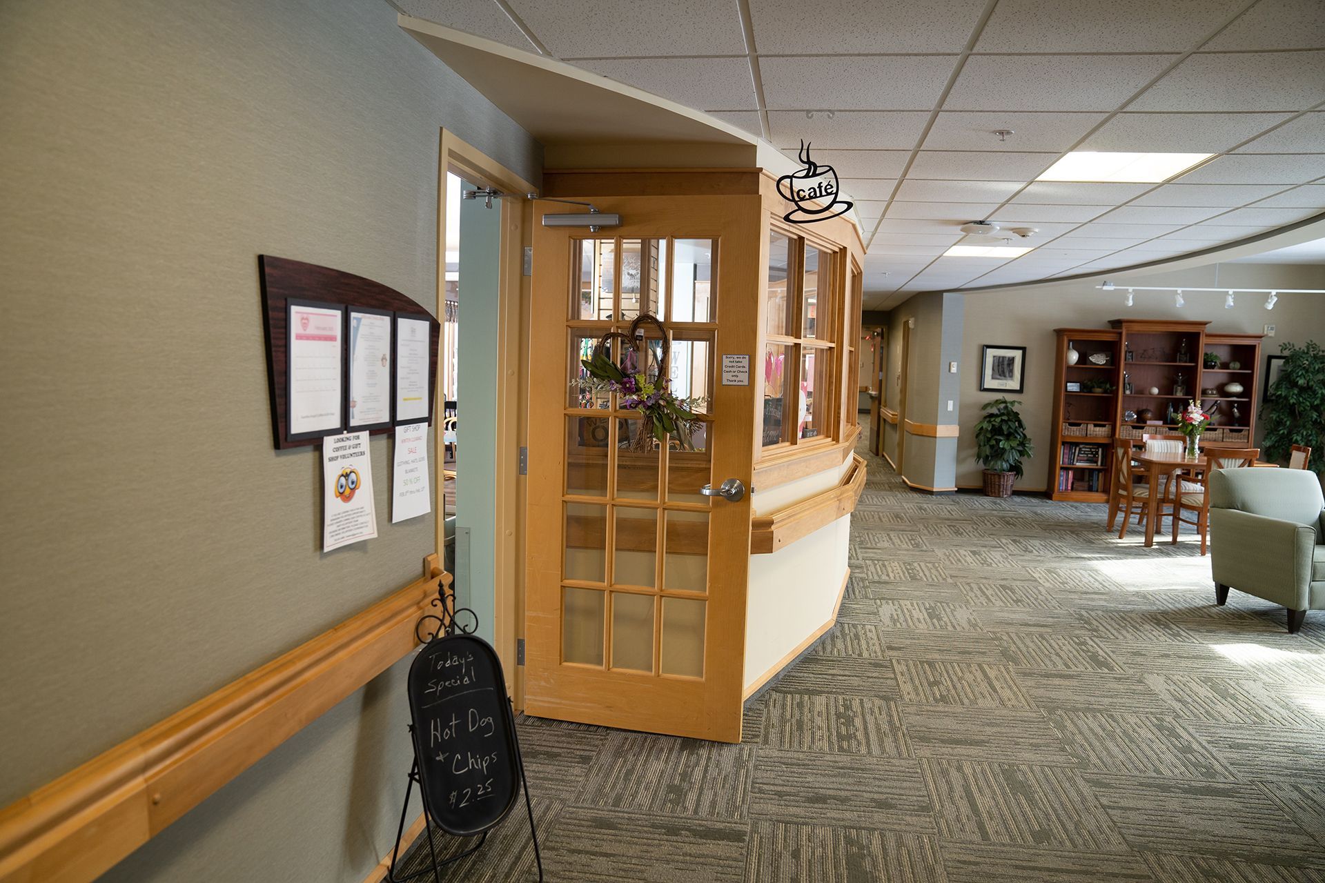 A wood-framed glass door, a hallway with carpet, a wall-mounted bulletin board, and a small sitting area in a lobby.