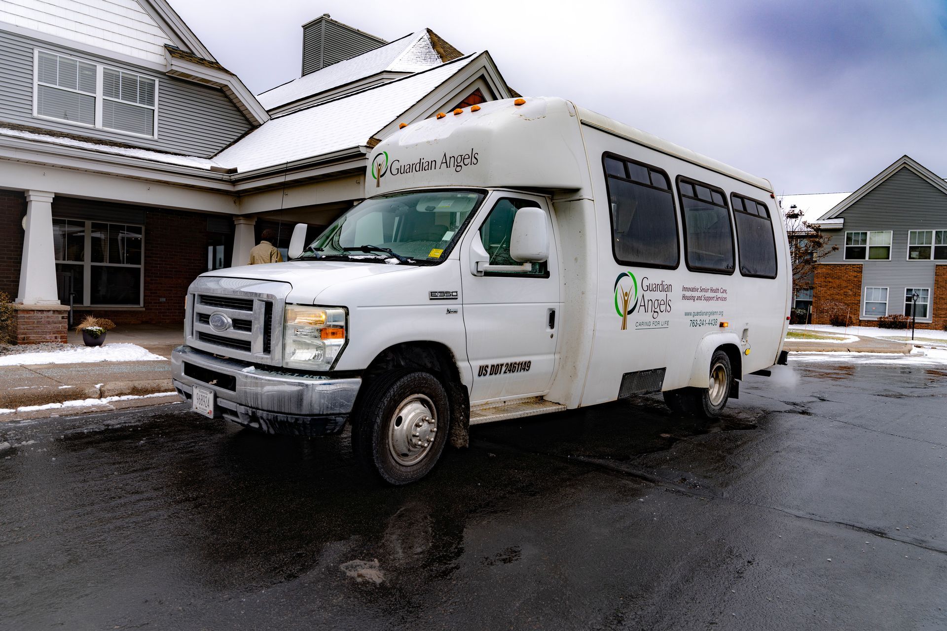 White shuttle bus parked on a snowy road in front of a residential building.