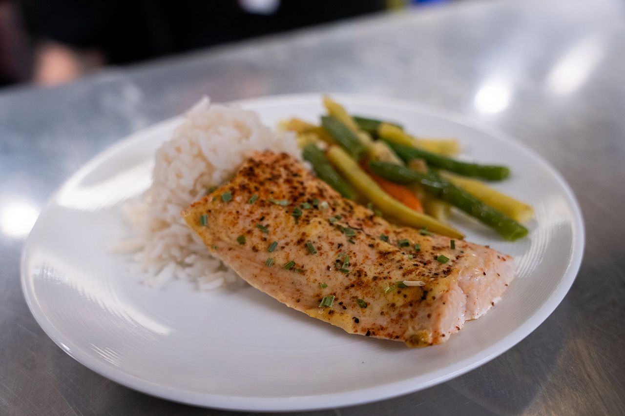 A plate containing a seasoned salmon fillet, a serving of white rice, and a mix of green and yellow string beans.