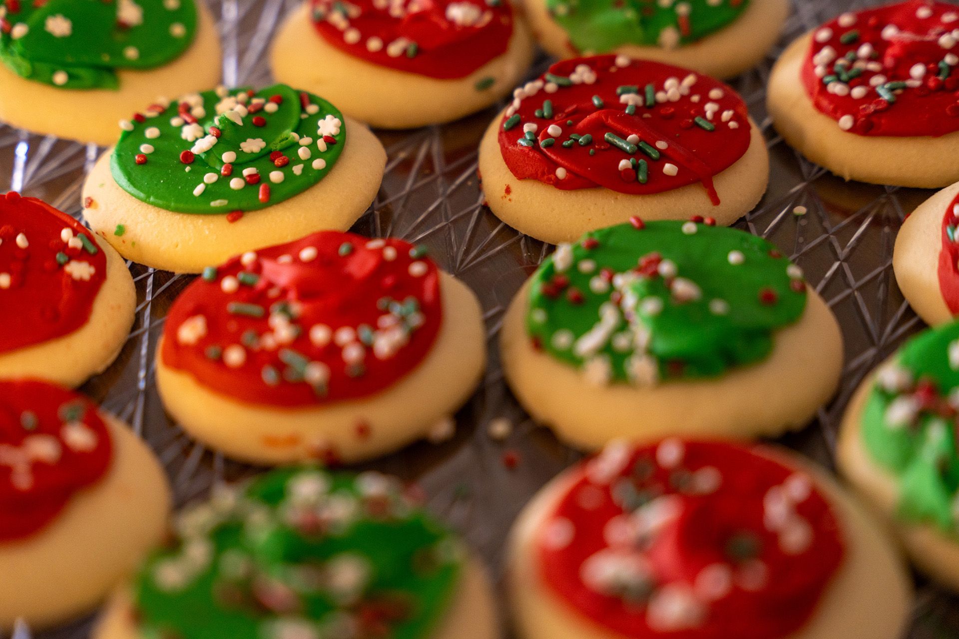 Round sugar cookies decorated with red and green icing and festive sprinkles, arranged on a glass serving platter.