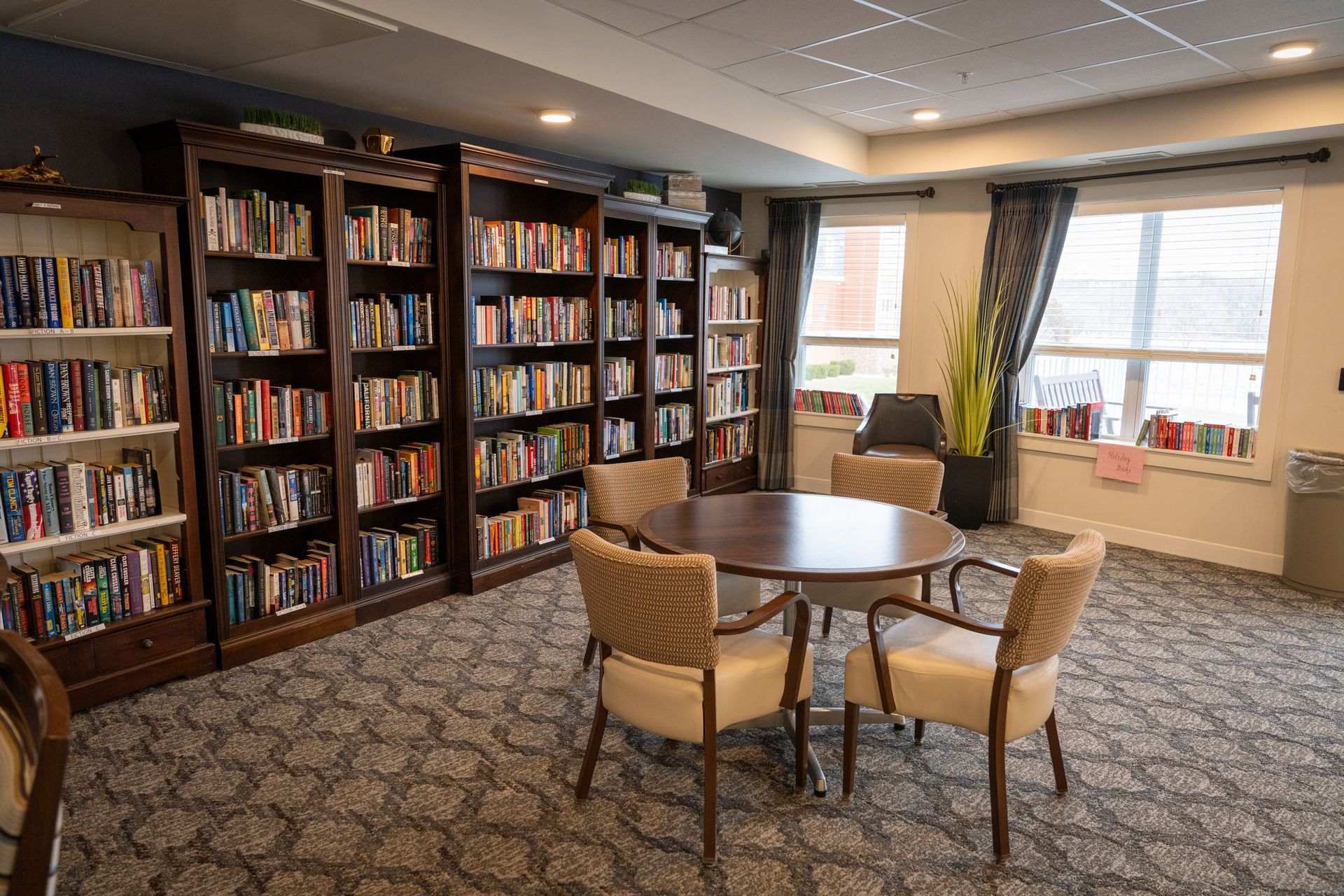 A library or lounge room with several dark wood bookcases filled with books, a round table, and four upholstered chairs.