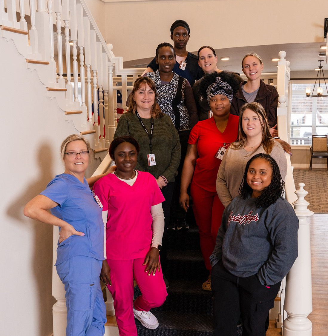 A group of staff members in scrubs and casual clothing posing together on a staircase indoors.