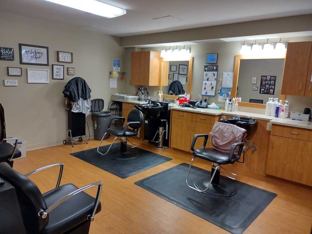 A brightly lit hair salon featuring three black styling chairs on floor mats, two washing stations, and wood cabinetry.