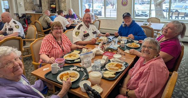 A group of people eating lunch at a long table in a bright community dining room.