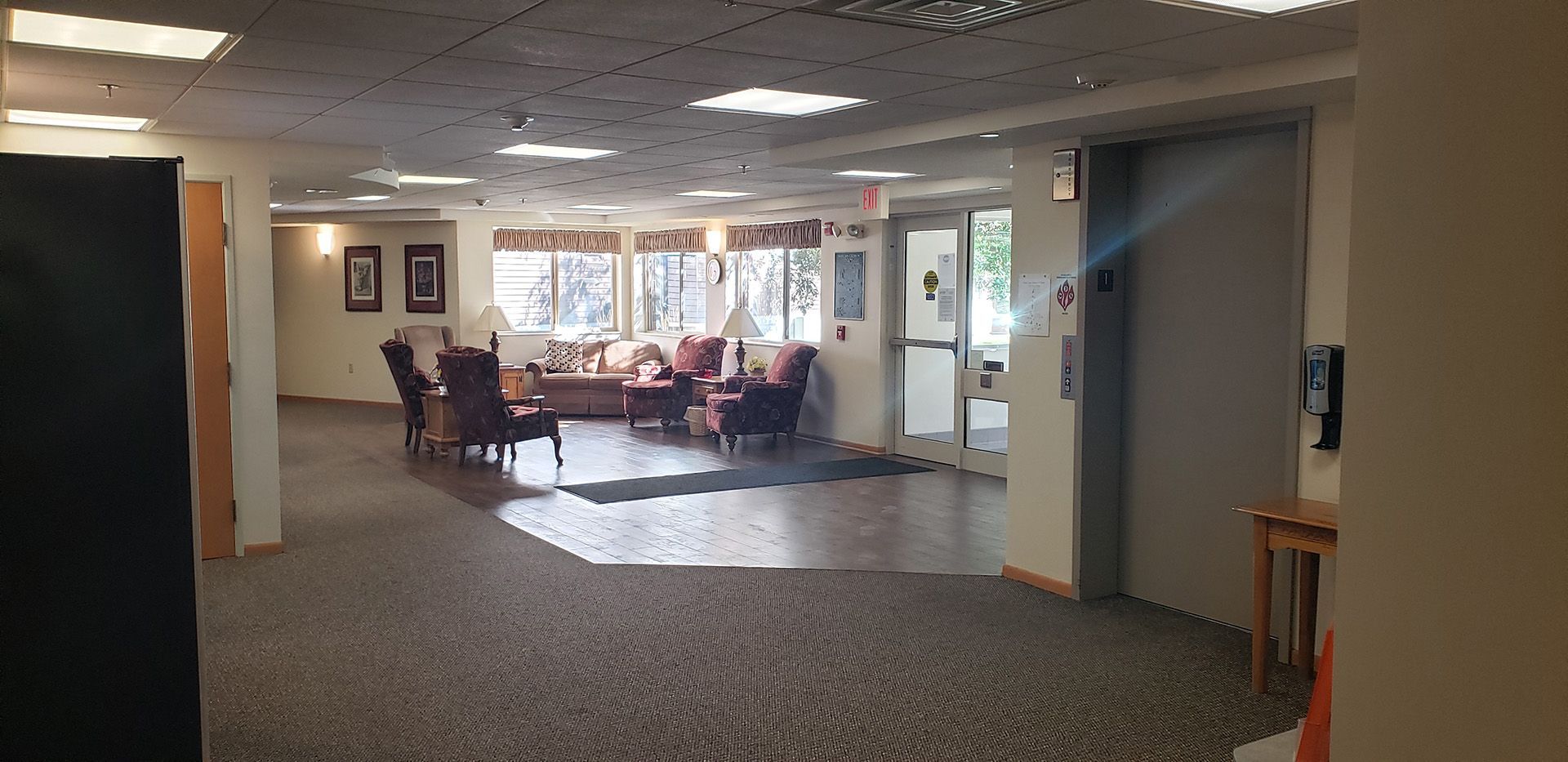 A lobby with a carpeted floor, seating area, glass entrance doors, and an elevator door.