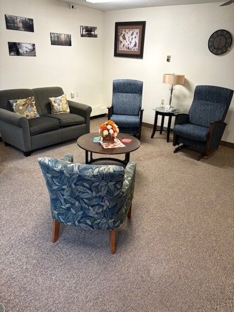 A comfortable waiting area featuring a grey sofa, two blue recliners, a patterned armchair, and a circular wooden table.
