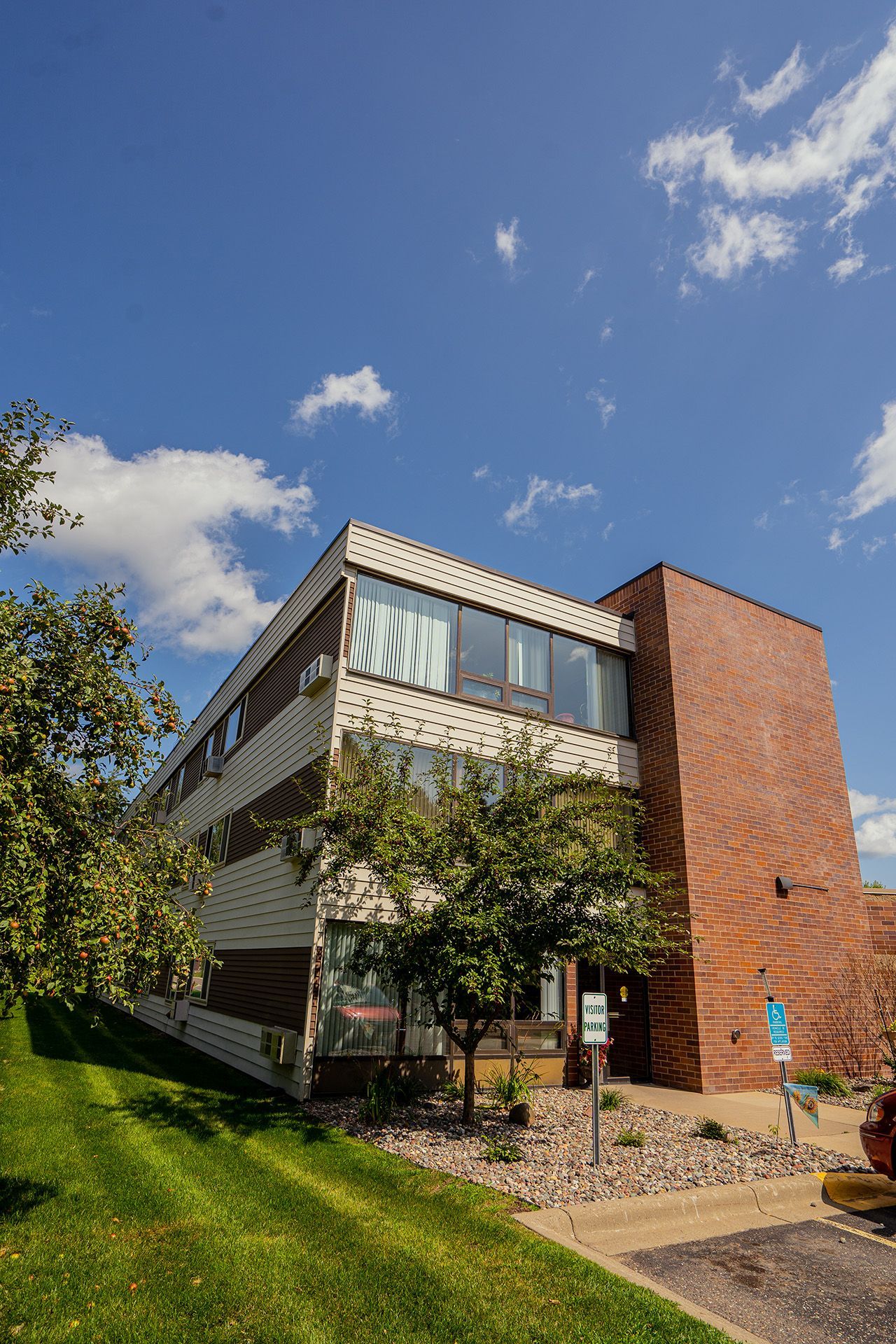 A three-story building with a brick facade on the right and beige exterior on the left, set against a bright blue sky.