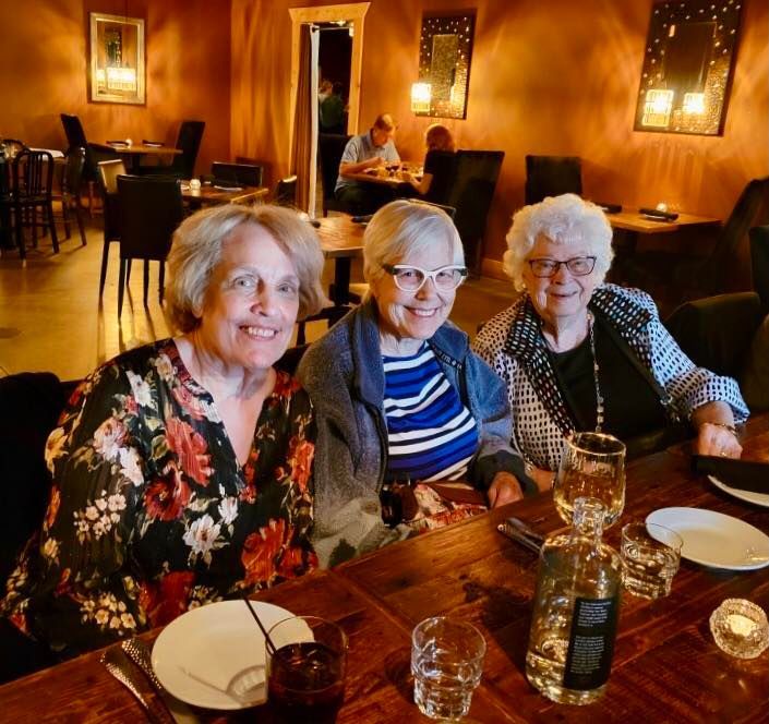 Three people smile while sitting at a rustic wooden table in a dimly lit restaurant.