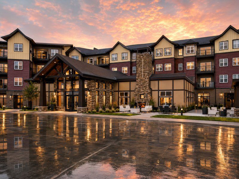 Modern lodge-style hotel exterior at sunset with wet pavement reflecting the building